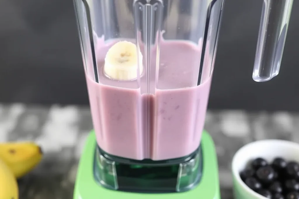 Blender in action, mixing almond milk, banana, blueberries, chia seeds, and honey into a creamy smoothie