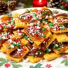 A tray of Christmas Cracker Candy with saltine crackers, toffee, melted chocolate, and festive toppings like crushed candy canes and sprinkles, presented on a holiday-themed plate with seasonal decorations