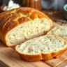 Golden-brown cottage cheese bread loaf sliced on a wooden cutting board, showing a soft, fluffy interior with herbs on top, set in a rustic kitchen with natural lighting