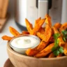 Close-up of golden-brown air-fried sweet potato fries served with garlic aioli in a rustic bowl, showcasing the perfect caramelized texture and crispiness