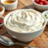 A bowl of creamy, homemade whipped cottage cheese surrounded by fresh toppings like berries, honey, and herbs, styled on a rustic wooden table