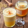 Lotus Seed Honey Drink in a glass, garnished with cardamom and saffron, with lotus seeds and honey jar in the background on a rustic table