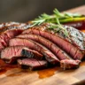 London Broil steak sliced thinly against the grain, served with grilled vegetables and fresh herbs, showcasing a tender, juicy interior and a golden-brown crust