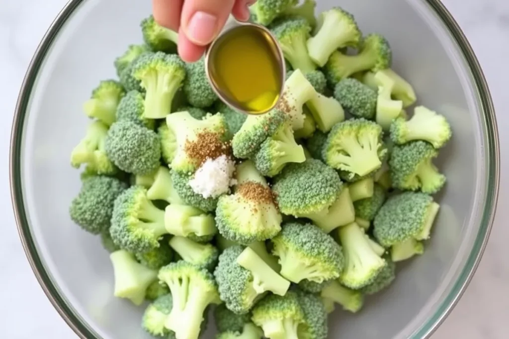 Frozen broccoli in a bowl being tossed with olive oil, garlic powder, salt, and pepper to enhance flavor before cooking