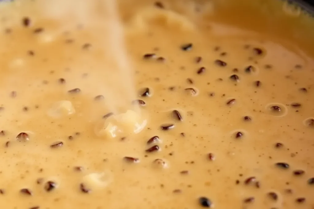 Peppercorn sauce simmering in a skillet, reaching a creamy, thick consistency for steak