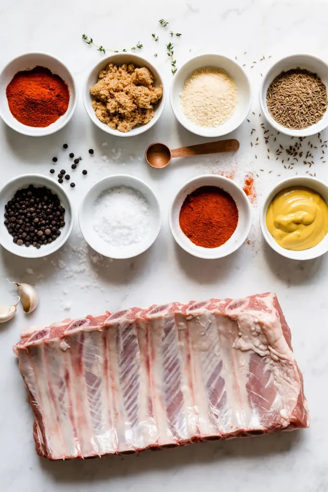 Dry rub ingredients for gas grill ribs including smoked paprika, brown sugar, garlic powder, and cumin on a marble surface