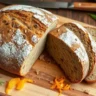 Swedish Limpa Rye Bread sliced to show its dense, moist texture, with caraway seeds, orange zest, and rye flour on top, styled in a rustic kitchen setting