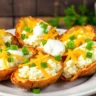 Golden-brown air fryer baked potato skins filled with creamy cottage cheese, cheddar, and green onions on a white plate