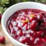 Homemade cranberry sauce with raspberry jam, garnished with fresh cranberries and orange zest, served in a bowl