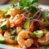 A vibrant plate of Garlic Shrimp Aguachile garnished with fresh avocado, cucumber, and red onion.