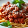 A delicious serving of Bolognese sauce over pasta with grated Parmesan cheese and fresh basil leaves