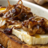 Close-up of Caramelized Onion and Brie Toast served on a rustic white plate with golden, melted Brie and caramelized onions