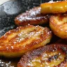 Skillet banana fritters served in a white dish with powdered sugar and honey drizzle