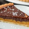 Close-up of Salted Caramel Chocolate Tart with glossy chocolate ganache, salted caramel, and buttery crust on a white plate.