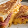 Close-up of a Classic Ham and Cheddar sandwich served on a white plate with melted cheddar cheese and crispy golden bread, captured with soft natural lighting.