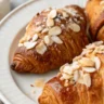 Close-up shot of almond croissants served on a white ceramic plate, showcasing flaky texture and almond topping.