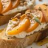 A close-up of Goat Cheese and Apricot Crostini served on a white plate, featuring toasted baguette slices topped with creamy goat cheese, fresh apricots, and a drizzle of honey.