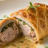 Close-up shot of Chicken Meatloaf Wellington served on a white plate with rich textures, flaky puff pastry, and golden crust