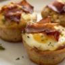 Close-up image of freshly baked Bacon and Egg Breakfast Muffins served on a plain white plate, showcasing the golden-brown bacon and melted cheese.