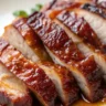 Chinese BBQ Pork slices on a plain white plate with a caramelized glaze, showcasing the tender and flavorful dish