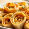 Close-up of Simple Cheesy Pinwheels served in a white dish, featuring golden-brown tortilla spirals filled with melted cheese