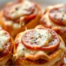 Close-up of golden-brown Pepperoni Pizza Bombs served on a white plate, featuring melted cheese and crispy edges.