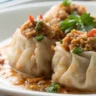 Kanom Jeeb Thai dumplings served in a white plate with soft natural lighting