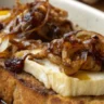 Close-up of Caramelized Onion and Brie Toast served on a rustic white plate with golden, melted Brie and caramelized onions