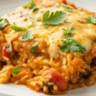 Top view of cheesy Chicken Enchilada Rice Casserole served on a plain white plate with beans, corn, and melted cheese, captured with natural lighting