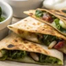 Golden baked spinach mushroom quesadillas sliced into wedges with cheese, spinach, and mushrooms inside, served on a white plate
