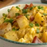 Cheesy Potato Egg Scramble served on a white plate with golden potatoes, soft eggs, and melted cheese