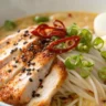 Close-up of Fiery Chicken Ramen with Creamy Garlic Sauce topped with egg, scallions, and chili oil in a white bowl