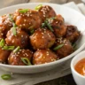 Close-up of Korean BBQ meatballs glazed with sticky sauce, sprinkled with sesame seeds and scallions, served with spicy mayo dip in a white bowl