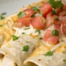 Close-up of creamy white chicken enchiladas topped with melted cheese and cilantro in a white serving dish