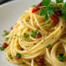 A plate of Spaghetti Aglio e Olio with golden garlic slices, chili flakes, and parsley on a white ceramic dish.