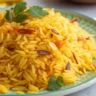 Persian Saffron Rice (Tachin) with a golden crispy tahdig crust, garnished with barberries and pistachios, served in a white plate on a wooden table