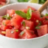 A top-view close-up of Honey-Lime Mint Watermelon Salad in a white bowl, garnished with fresh mint and lime zest