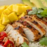 Overhead view of Chili Lime Mango Marinated Chicken Bowls with grilled chicken, mango, avocado, and rice served in a white bowl