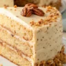 Close-up of a moist Butter Pecan Layer Cake with toasted pecans and creamy buttercream frosting on a white plate