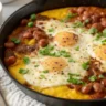Top-down view of Polenta Refried Beans and Egg Skillet Bake in a white plate with golden polenta, creamy beans, baked eggs, and cilantro