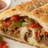 Close-up of sliced sausage pepper and onion stromboli showing melted mozzarella, cooked Italian sausage, and sautéed peppers and onions on a golden baked crust