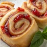 Close-up of Strawberry Rhubarb Basil Jam Rolls with swirls of jam and basil on a white plate