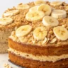 A close-up photo of a moist cake with oat flakes and bananas served on a white plate