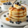 Fluffy golden pancakes stacked high with butter, maple syrup, and blueberries for National Pancake Day celebration