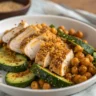 Close-up overhead photo of Chicken Shawarma with Chickpeas and Dukkah Courgettes on a white plate with chickpeas and dukkah courgettes.