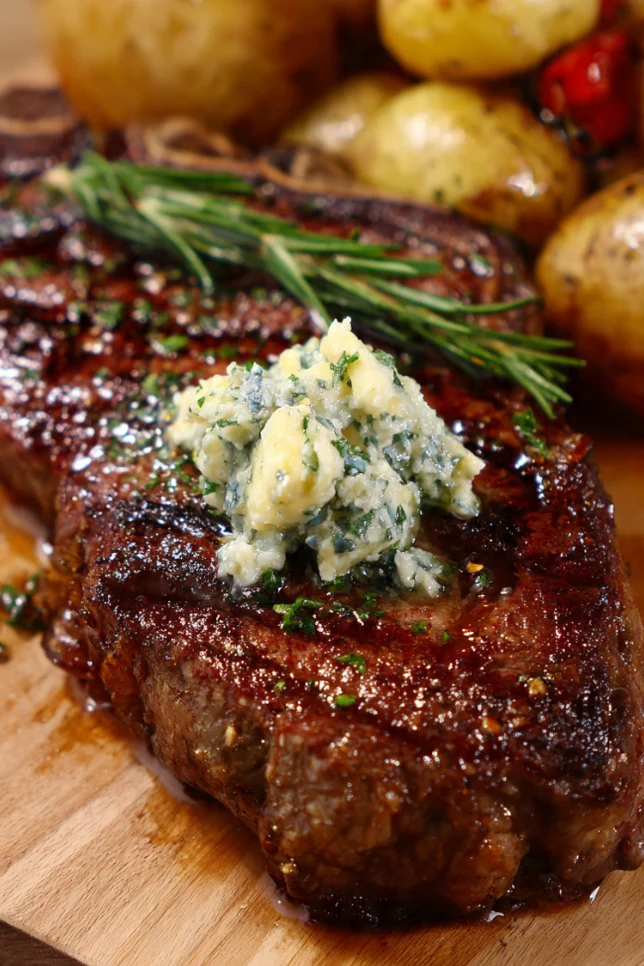 Perfectly seared cowboy steak with melting truffle honey butter on a dark wooden cutting board, sliced to show medium-rare interior