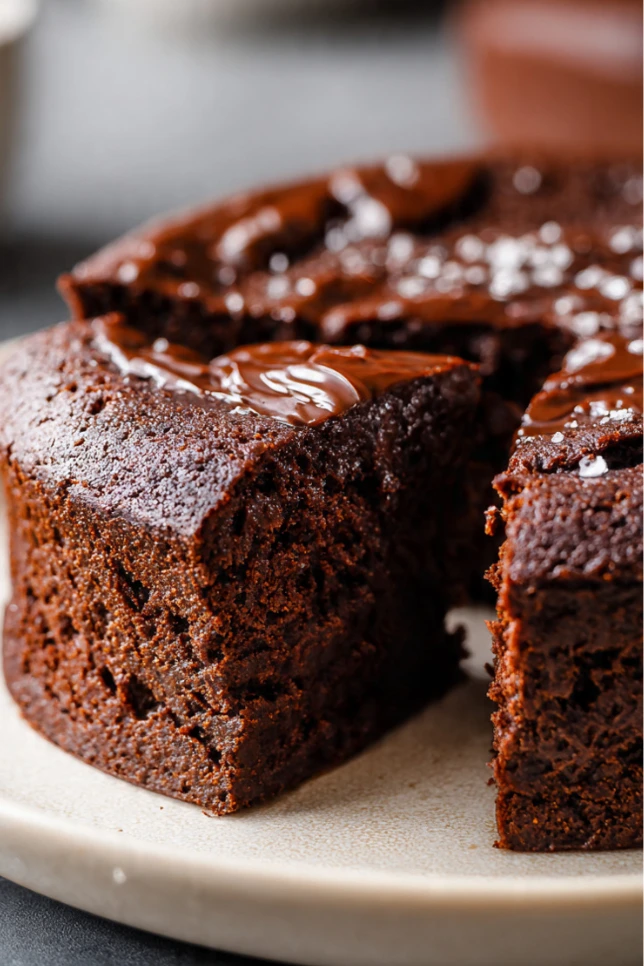 Fudgy 3-ingredient healthy chocolate cake on white plate with slice cut showing moist texture