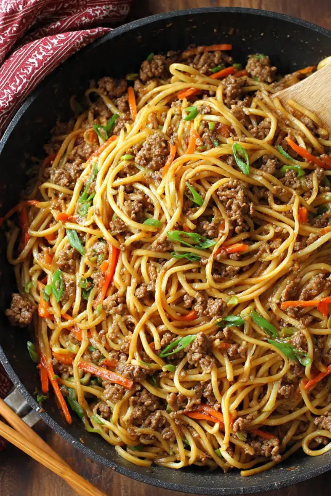 Bowl of ground beef lo mein with noodles, vegetables, and chopsticks on wooden table