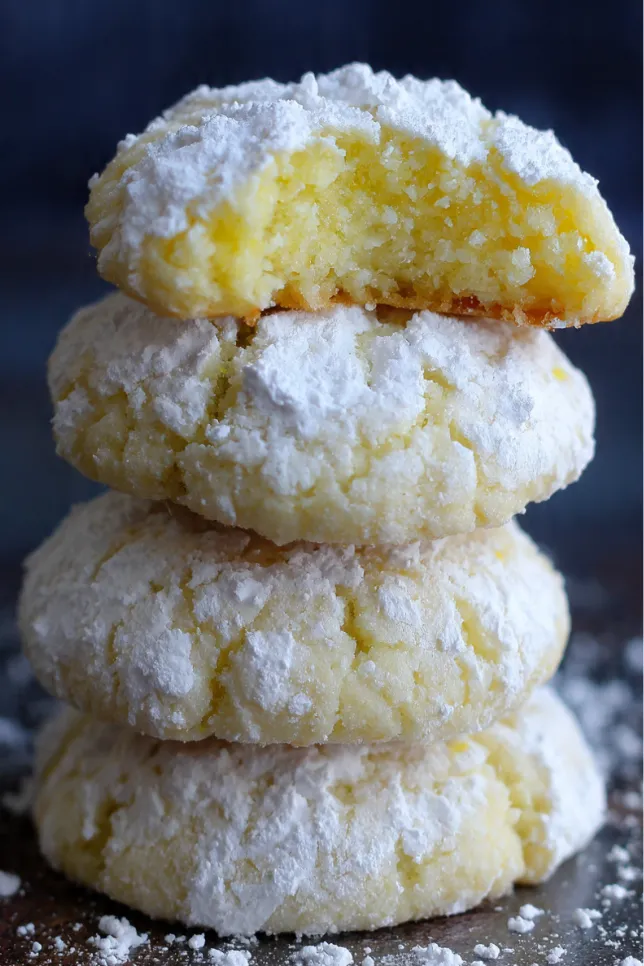 Powdered sugar-coated lemon meltaway cookies stacked on white plate with fresh lemons