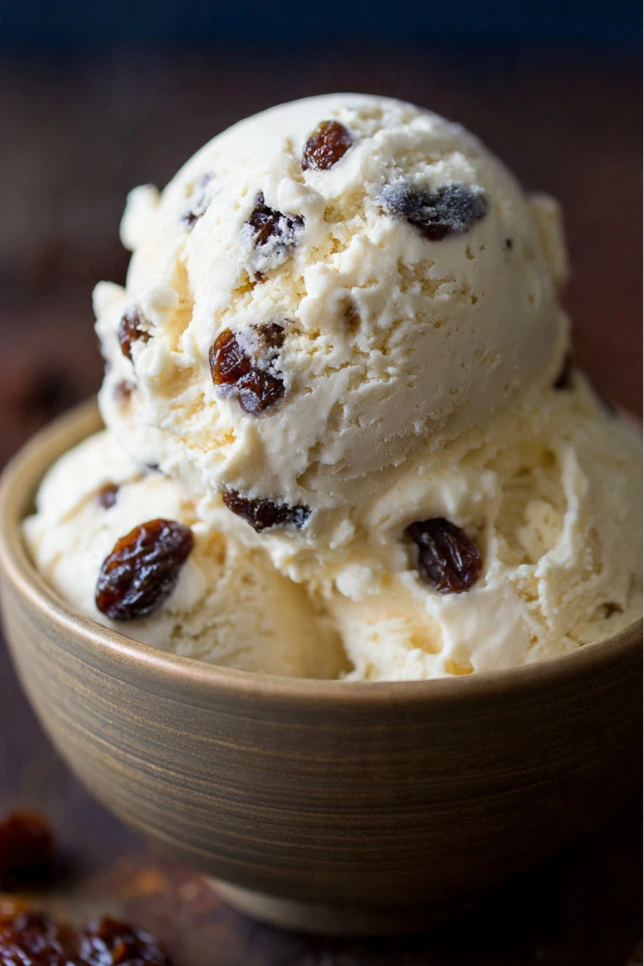 Scoop of homemade Jamaican rum raisin ice cream in ceramic bowl with dark rum-soaked raisins